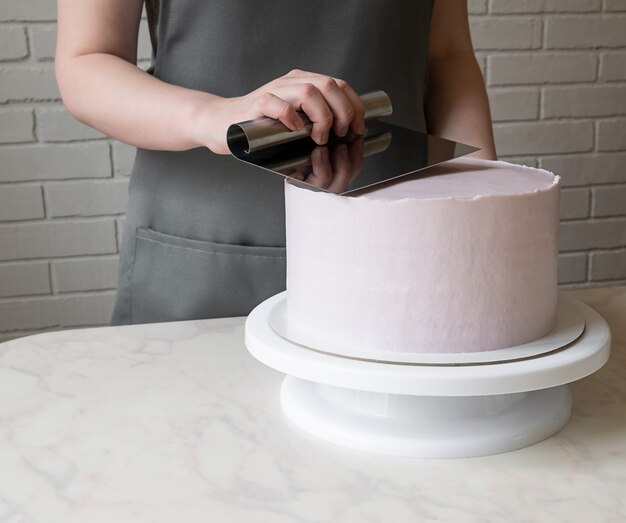 Ligne de mains de fille avec une spatule à crème sur un gâteau rond. décorer le gâteau des fêtes.