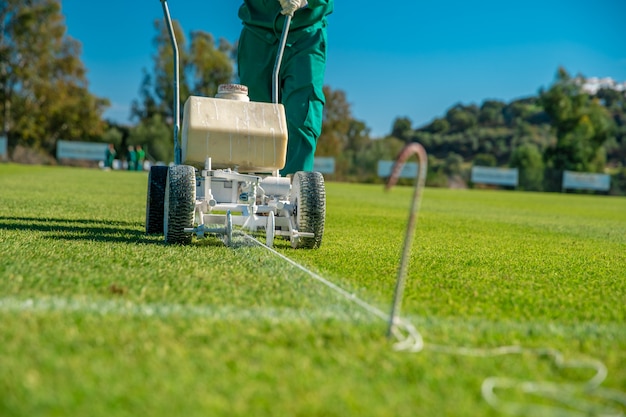 Lignes blanches tracées sur le terrain de football avec de la peinture blanche sur l'herbe à l'aide d'une machine spéciale avant un match
