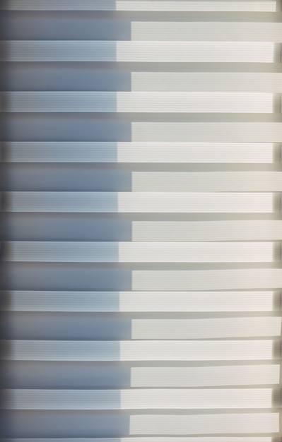 Lignes horizontales géométriques abstraites couleur dégradé blanc et gris. Motif répétitif, texture d'arrière-plan, conception de lignes rayées. Volets roulants éclairés par le soleil, gros plan.