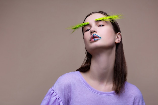 Lignes sur les lèvres. Modèle professionnel aux yeux noirs avec des lignes bleues sur les lèvres posant avec un épillet vert