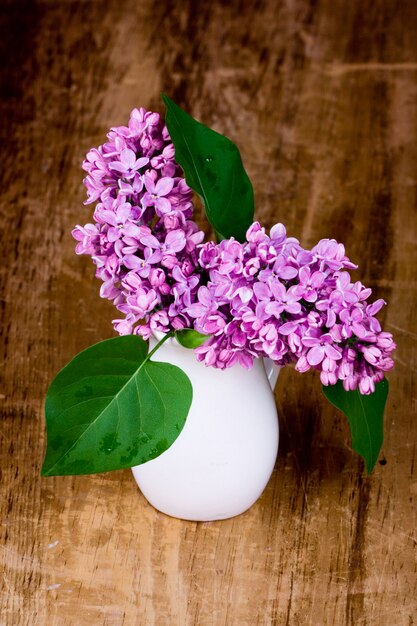 Lilas fleurit dans un petit vase blanc sur une table en bois