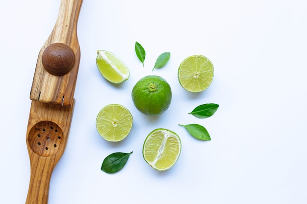 Limes avec presse citron vert en bois sur blanc.