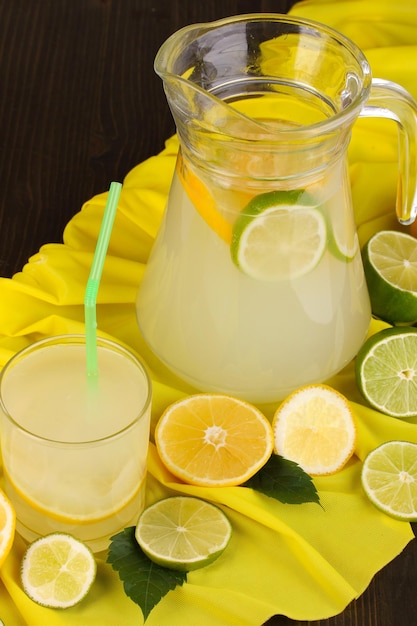 Limonade aux agrumes en verre et pichet d'agrumes autour sur tissu jaune sur table en bois gros plan