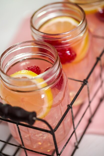 Photo limonade aux framboises dans des bocaux mason sur un tableau blanc.