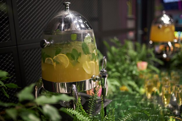 Photo limonade dans un distributeur sur une table décorée d'herbes fraîches et de fleurs