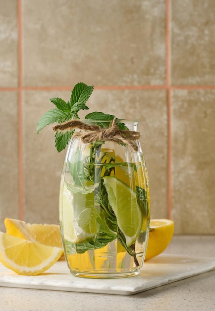 Limonade dans un verre transparent avec des brins de romarin au citron vert et des feuilles de menthe sur fond blanc