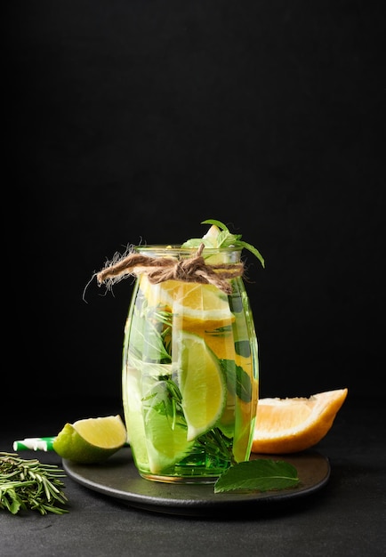 Limonade dans un verre transparent avec des brins de romarin au citron vert et des feuilles de menthe sur fond noir