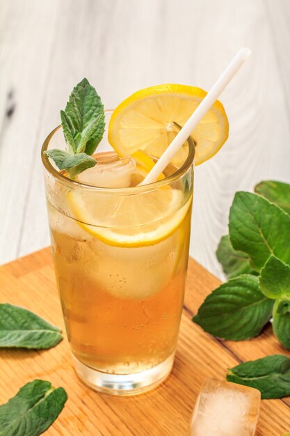 Limonade d'été rafraîchissante froide avec de la glace et des tranches de citron, décorée de feuilles de menthe dans un grand verre sur une planche à découper et un fond en bois gris