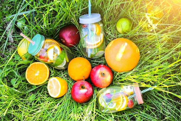 Limonade fraîche dans des bocaux avec des pailles. Boissons d'été hipster avec des fruits dans l'herbe verte à l'extérieur. Respectueux de l'environnement dans la nature. Citrons, oranges et baies à la menthe dans le verre. Mode de vie végétalien sain.