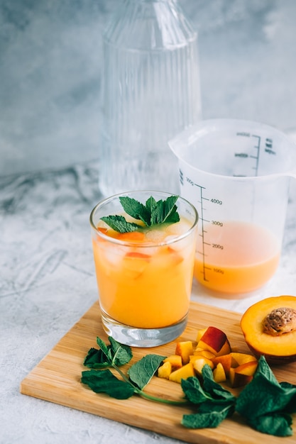 Limonade glacée en verre avec morceaux de pêche, menthe fraîche et glaçons sur la table