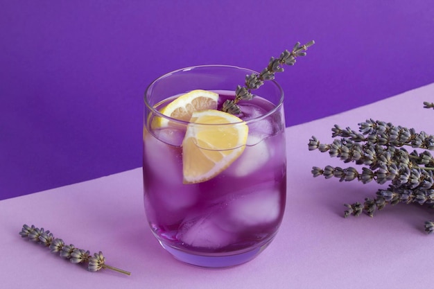 Limonade à la lavande avec glace et citron dans le verre à boire sur fond violet. Fermer.