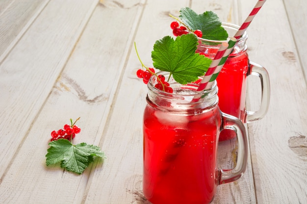 Limonade maison aux groseilles dans un bocal avec décor de baies sur une table en bois claire.