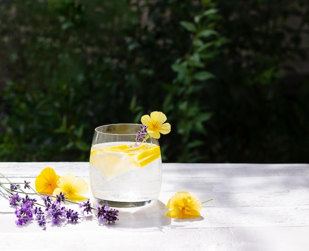 Limonade maison avec citron et glaçons dans un verre sur la table en bois blanc avec fleurs jaunes et lavande