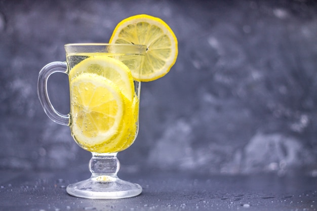 Photo limonade maison dans un verre avec une poignée sur un fond de béton gris. eau avec des tranches de citron