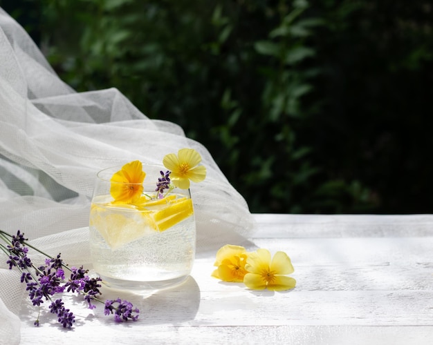 Limonade maison dans un verre sur la table en bois blanc avec fleurs jaunes et lavener avec tissu de tulle sur le fond