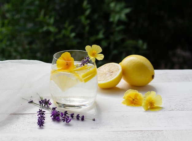 Limonade maison dans un verre sur la table en bois blanc avec fleurs jaunes et lavener avec tissu de tulle sur le fond