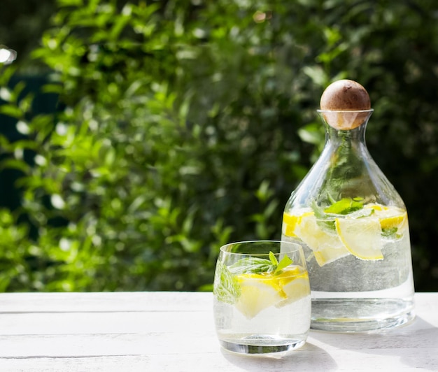 Limonade maison à la menthe citronnée et glaçons dans un pichet en verre sur la table en bois blanc