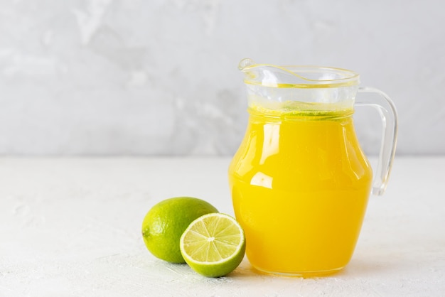 Limonade orange avec des tranches de citron vert dans une cruche sur une table lumineuse