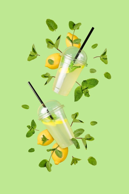 Photo limonade rafraîchissante volante dans des gobelets en plastique avec des citrons volants et des feuilles de menthe sur fond vert