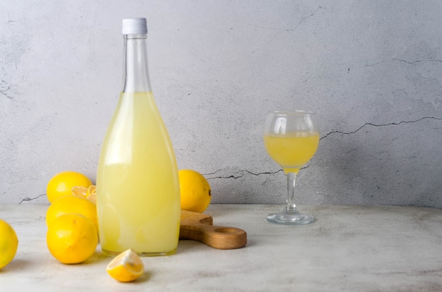 Limoncello en bouteille de verre et citrons jaunes mûrs frais sur fond gris, liqueur de citron italienne douce maison traditionnelle, boisson alcoolisée forte et citrons jaunes mûrs frais.