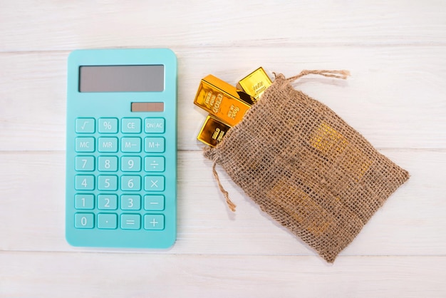 Lingots d'or dans un sac et une calculatrice sur un fond en bois blanc. Vue d'en-haut.