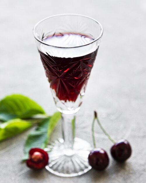 Liqueur de cerise dans un verre et fruits frais sur un fond de béton gris