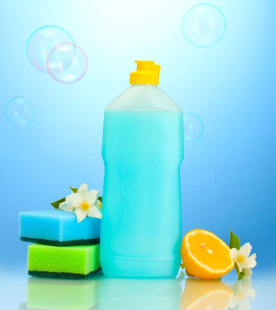 Photo liquide de lavage de vaisselle avec des éponges et du citron avec des fleurs sur fond bleu