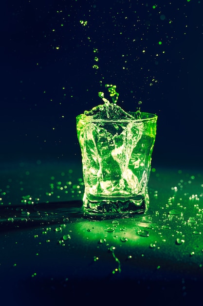 Liquide transparent de couleur verte éclaboussant hors de verre sur bleu foncé