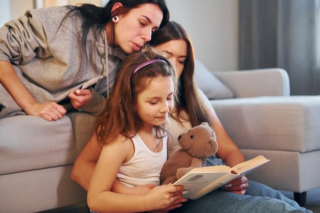 Lire un livre ensemble Couple de lesbiennes avec une petite fille passer du temps ensemble à la maison