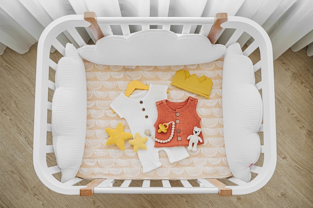 Photo lit bébé en bois blanc avec oreillers en forme de nuages dans la chambre de bébé. vêtements et accessoires pour nouveau-nés en lit bébé. vue de dessus du lit d'enfant