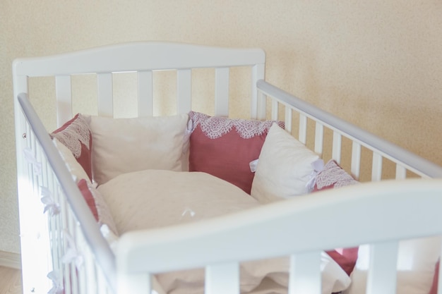 Photo lit de bébé avec des oreillers blancs et de couleur bourgogne avec des lacets