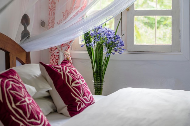 Lit douillet confortable dans la chambre et bouquet de fleurs près de la fenêtre en gros plan