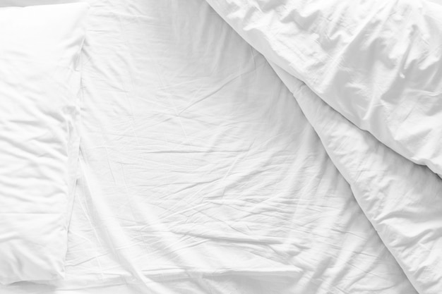 Lit non façonné avec un drap de lit froissé, une couverture et des oreillers après le sommeil de sommeil de confort, réveiller le matin