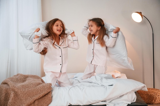 Sur le lit avec des oreillers Deux petites filles jouent et s'amusent ensemble dans la chambre domestique