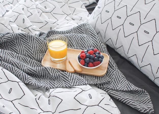 Lit de petit déjeuner Plateau en bois Intérieur matinal avec draps géométriques et taie d'oreiller Baies Jus d'orange