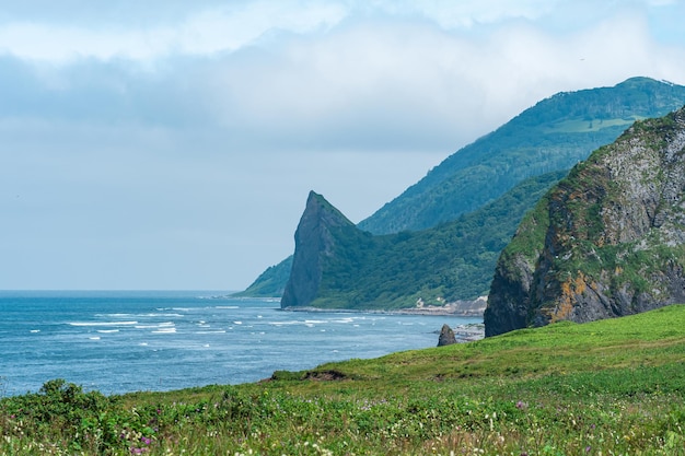 Littoral de l'île de Kunashir avec falaise de basalte et montagnes boisées dans les nuages