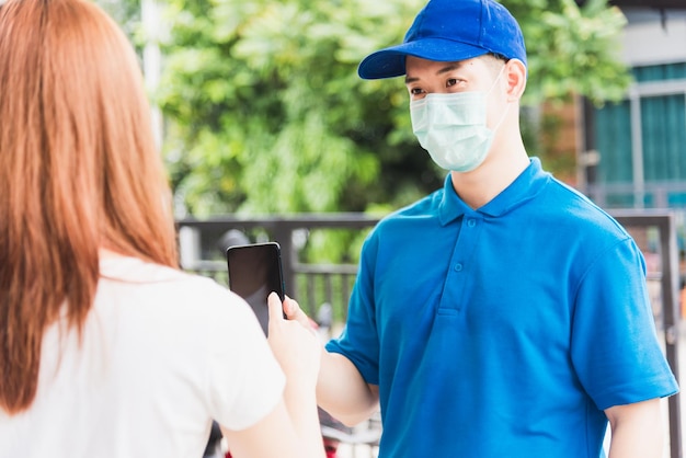 Livraison asiatique courrier express jeune homme donnant des boîtes de colis à la signature d'une cliente pour recevoir sur téléphone portable à la fois un masque protecteur, sous couvre-feu coronavirus pandémique de quarantaine COVID-19