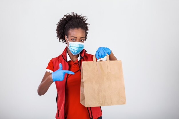 Livraison Femme Employée En T-shirt Rouge Uniforme Masque Gant Tenir Le Paquet De Papier Craft Avec De La Nourriture