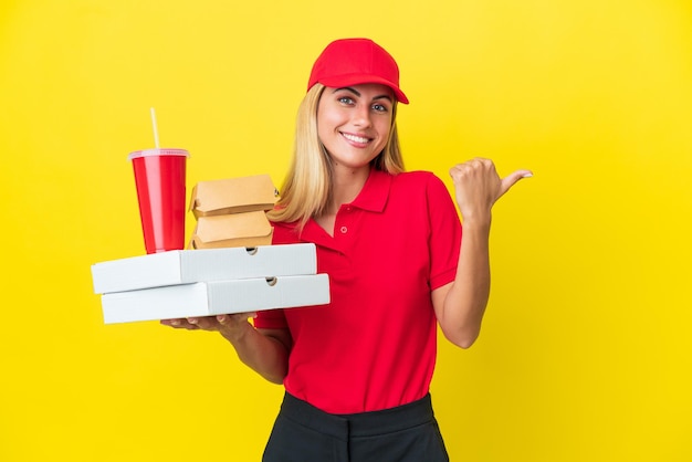 Livraison Femme uruguayenne tenant une restauration rapide isolée sur fond jaune pointant vers le côté pour présenter un produit