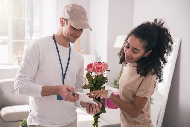 Photo livraison de fleurs. agréable femme agréable regardant l'écran de la tablette tout en confirmant la livraison