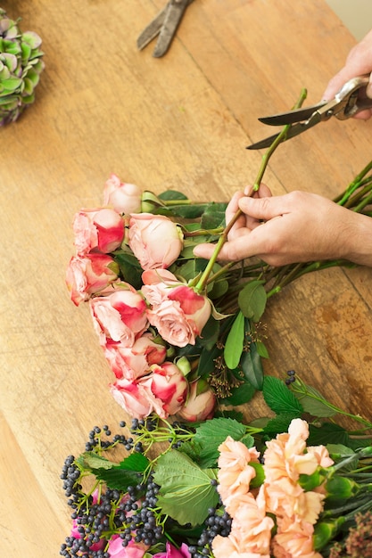 Photo livraison de fleurs, création de commande. les mains du fleuriste coupent la rose pour le bouquet en magasin de fleurs
