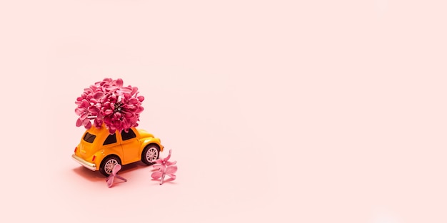 Livraison de fleurs fraîches pour les vacances. Voiture jaune jouet avec branche de fleur lilas.