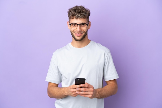 Livraison homme caucasien isolé sur fond violet envoyant un message avec le mobile