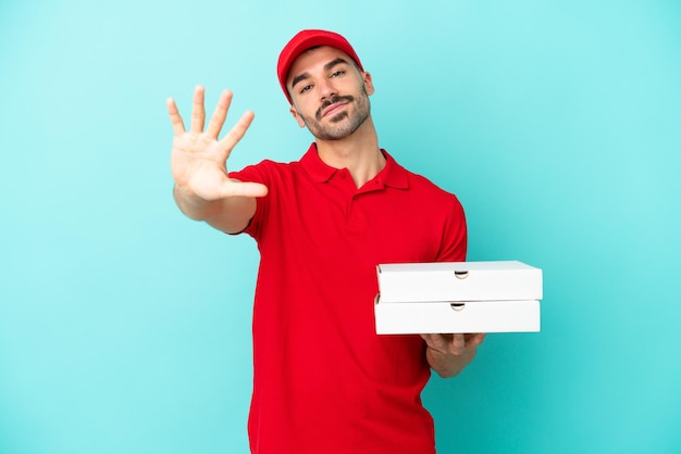 Livraison homme caucasien ramassant des boîtes à pizza isolées sur fond bleu en comptant cinq avec les doigts