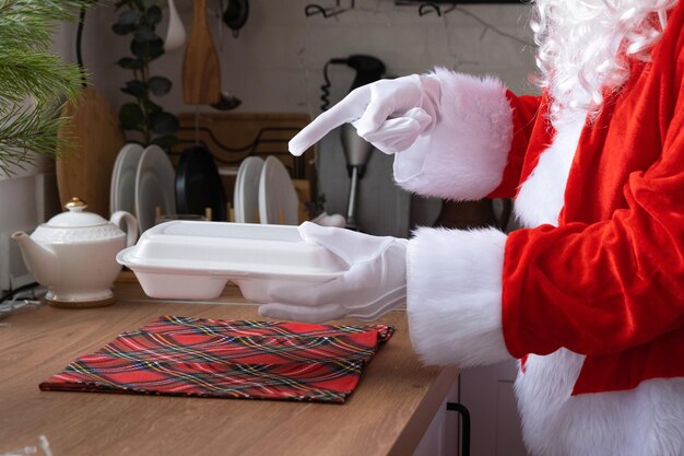 La livraison de nourriture dans des conteneurs de service à domicile entre les mains du Père Noël le met sur la table de la cuisine et l'emporte Commande chaude prête à l'emploi Noël Nouvel an vacances restauration