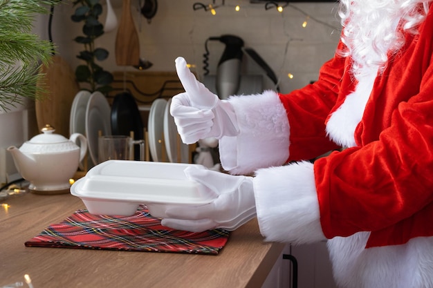 La livraison de nourriture dans des conteneurs de service à domicile entre les mains du Père Noël le met sur la table de la cuisine et l'emporte