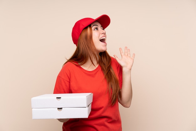 Livraison de pizza adolescent femme tenant une pizza sur un mur isolé avec une expression faciale surprise