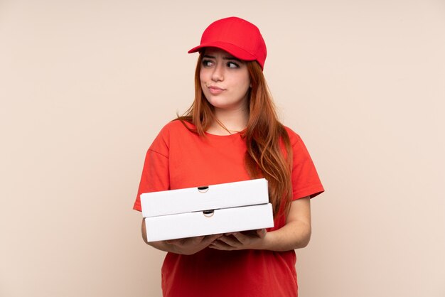 Livraison de pizza adolescent fille tenant une pizza sur le mur isolé en pensant à une idée