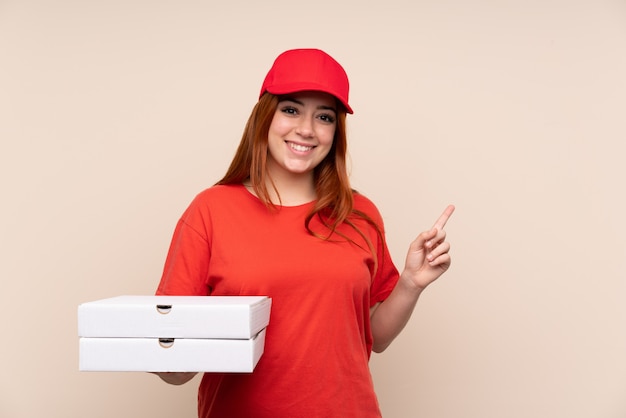 Livraison de pizza adolescent fille tenant une pizza sur le mur isolé pointant le doigt sur le côté