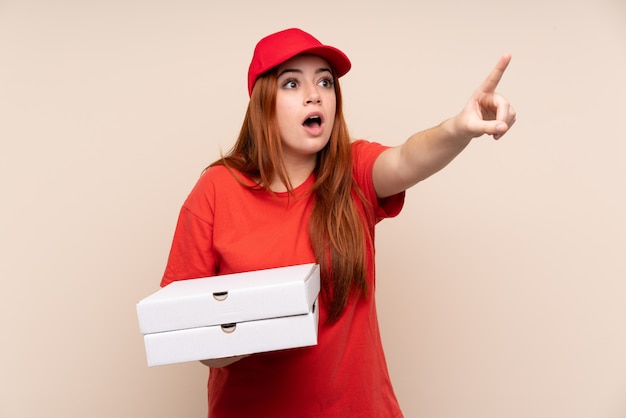 Livraison de pizza adolescent fille tenant une pizza sur un mur isolé pointant loin